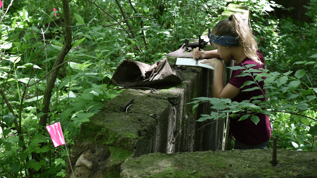 A student takes notes on an old foundation in the woods