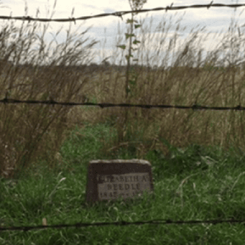 photo of a historic grave marker behind a barbed wire fence