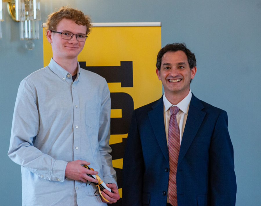 A young man holds a scroll, standing next to an older man in a suit