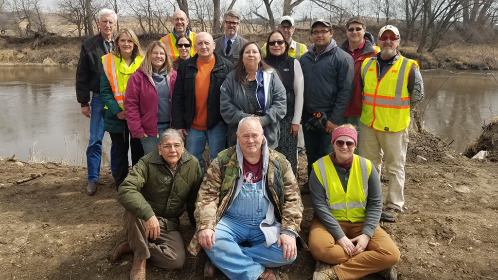 A group of people in fieldwork clothes and high visibility guests post along a river bank