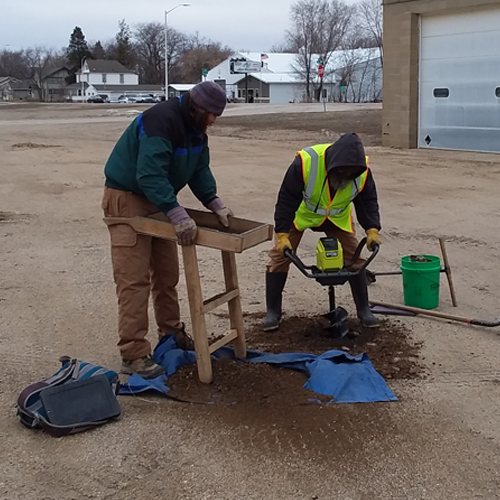2 men dig an auger soil test in a gravel lot