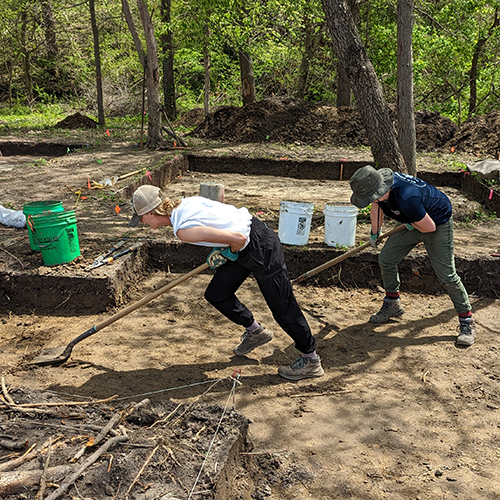 Two archaeologists skimming soil with shovels
