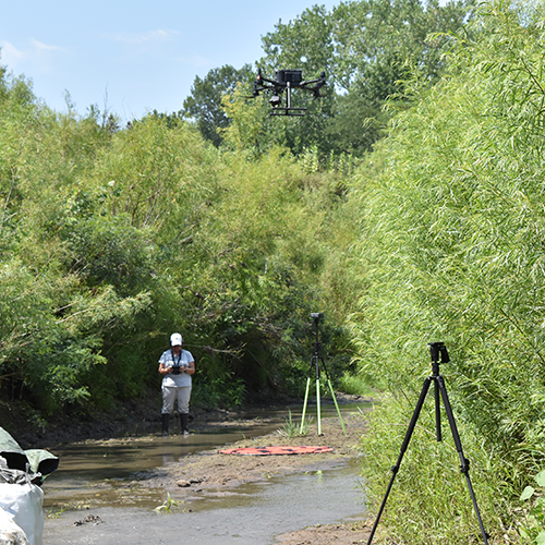 A woman standing in a creek while operating a drone