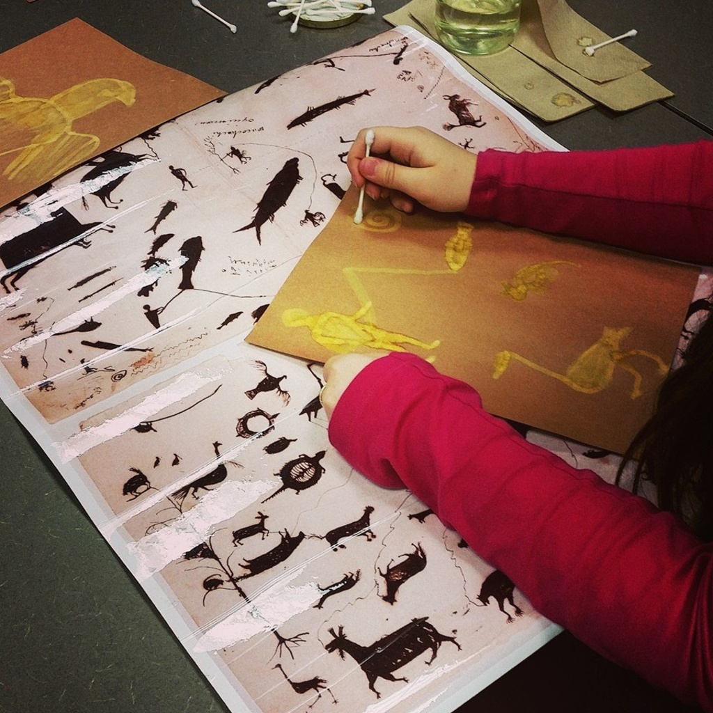 A child's arms; she is drawing pictographs