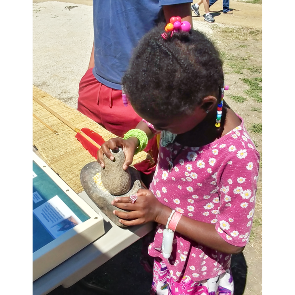 Photo of a young girl in a pink outfit grinding corn on with a mano and metate
