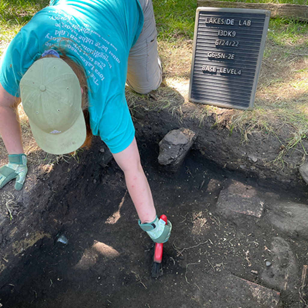 an archaeologist brushes the dirt in an excavation unit