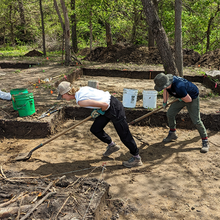 Two archaeologists skimming soil with shovels