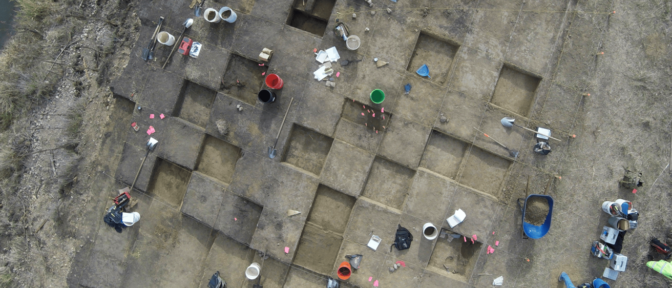 An aerial photo of a large excavation block with archaeological tools scattered about