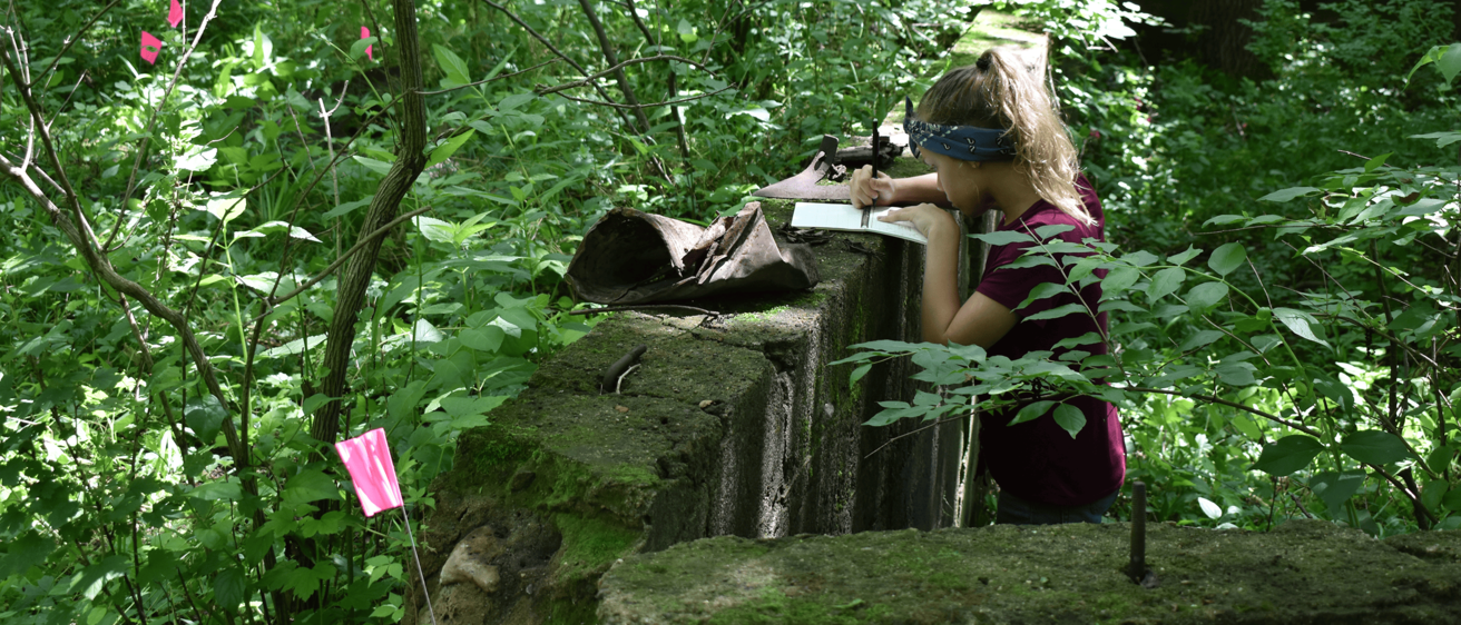 A student takes notes on an old foundation in the woods
