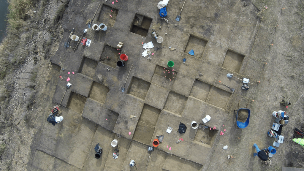 An aerial photo of a large excavation block with archaeological tools scattered about