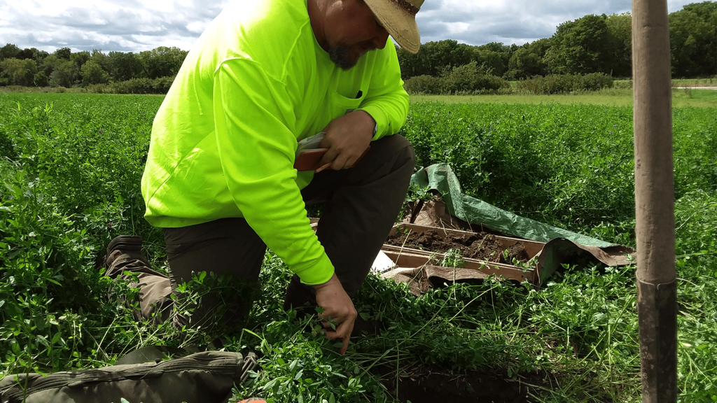A man in a neon yellow shirt digging a hole in a field