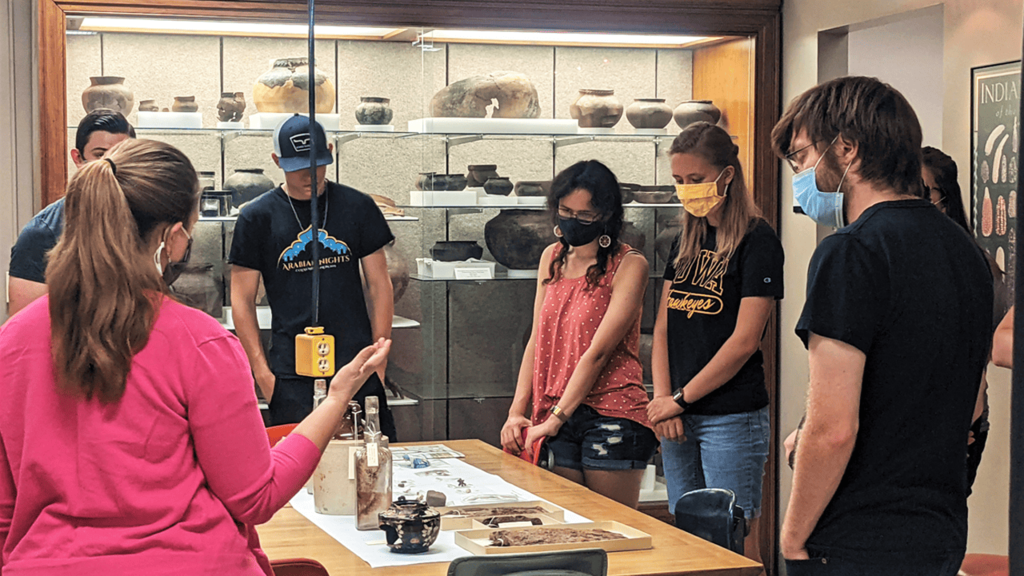 Adults wearing masks stand around a table looking at artifacts