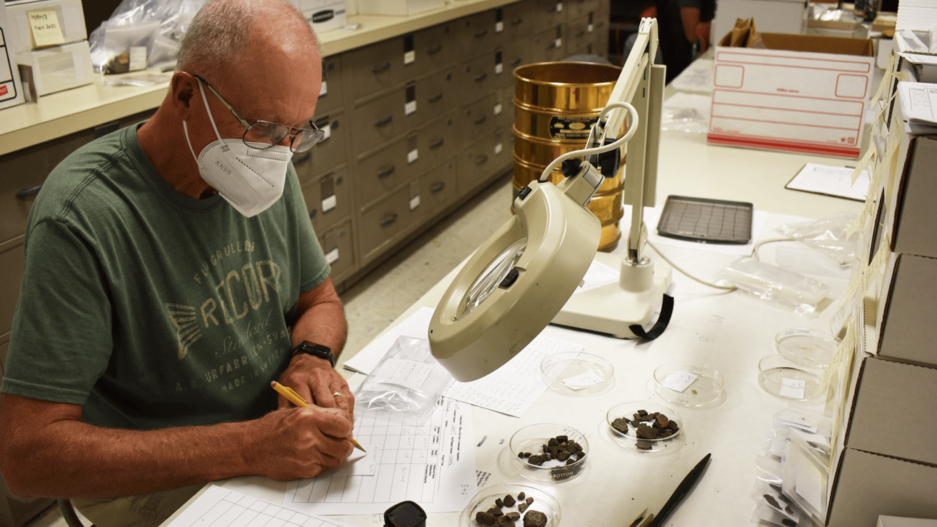 A man in a KN95 masks sorts fish bone at a lab table